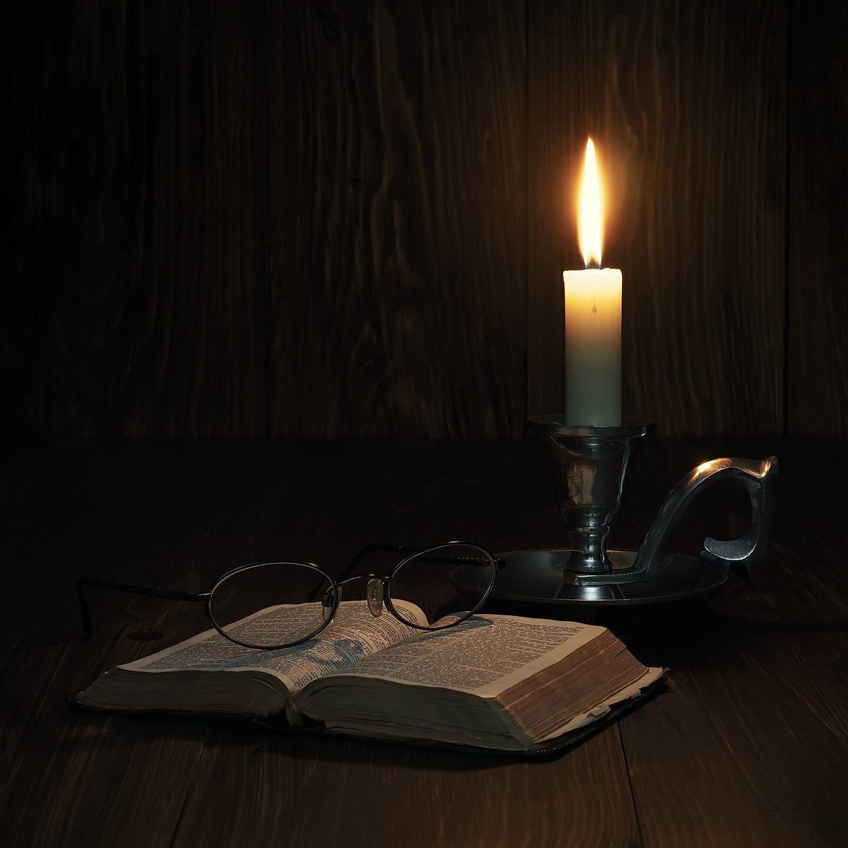 Библия рядом с горящей в темноте свечой