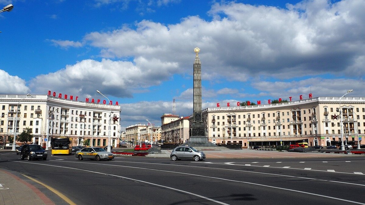 Здания и монумент на Площади Победы на фоне серых облаков и голубого неба